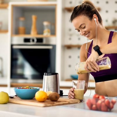 Young happy athletic woman having a fruit smoothie for breakfast in the kitchen.